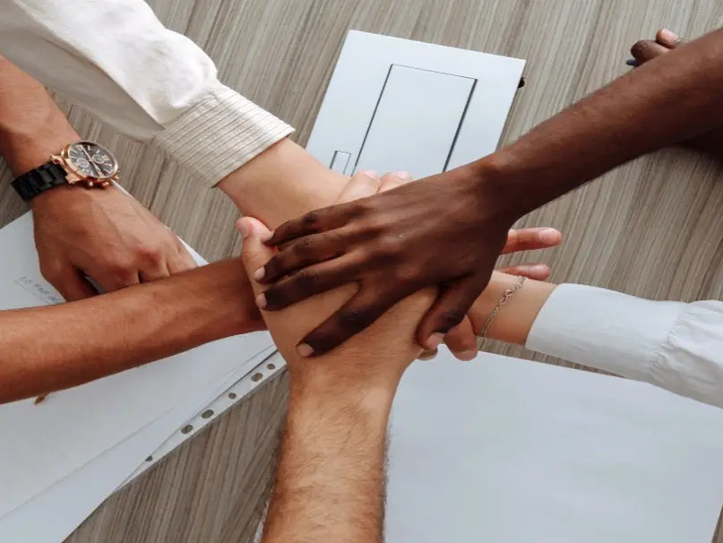 The hands of five team members are stacked on top of one another to symbolize teamwork.