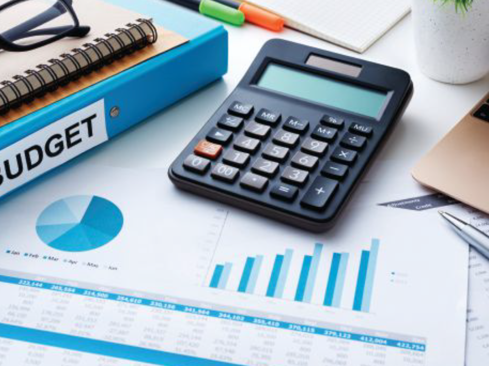 A calculator sits on a desk with financial papers, books and highlighters.