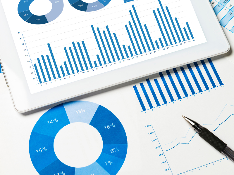 Pie charts and bar graphs containing data and statistics numbers. The charts are blue and white and a mix of paper and tablet on a table.