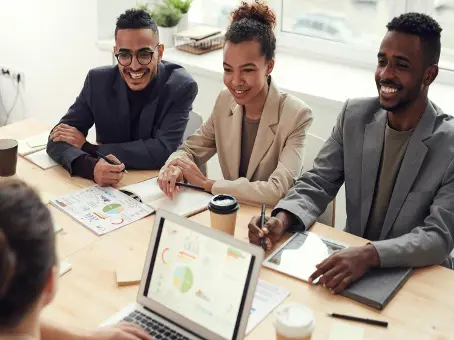 A group of 3 young employees sitting at a desk during a meeting.