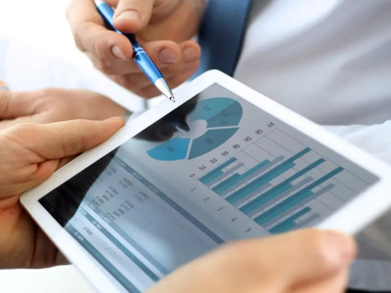 Graphs and a pie charts on the screen of an ipad held by a man in a suit.