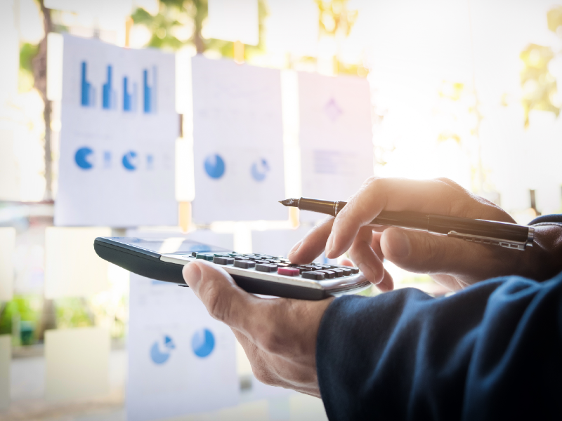 Hands of a business man with a calculator and graphs and charts in the background.