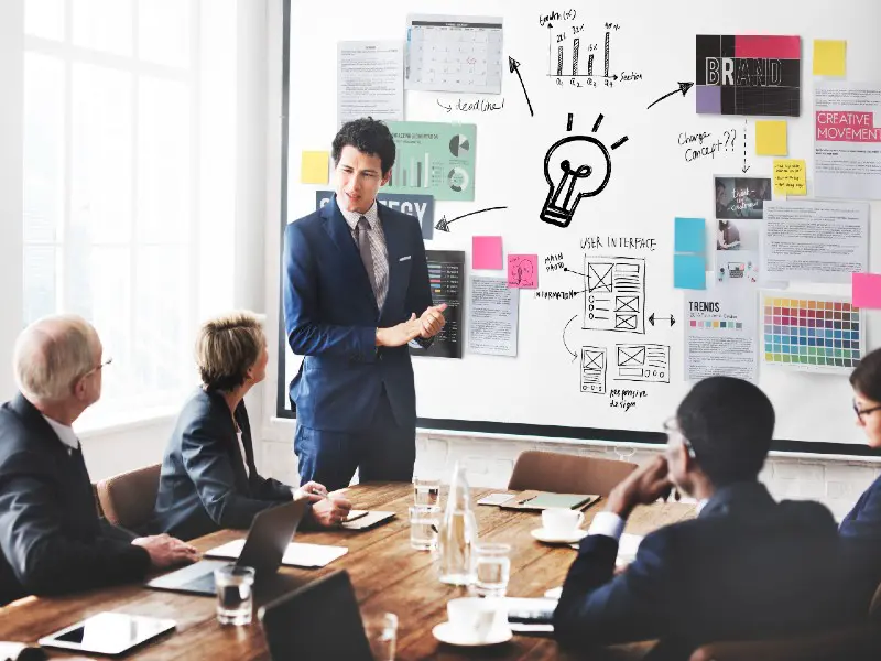 A young man in a suit presenting his ideas in a meeting as his team mates listen.