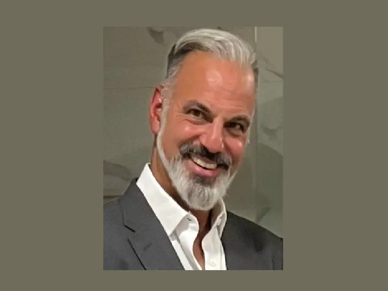 A man with short grey hair wearing a white button up shirt and grey suit jacket.