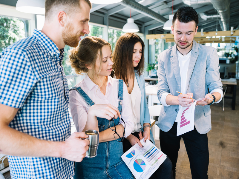 A group of young professionals discussing charts and graphs during an informal office meeting.