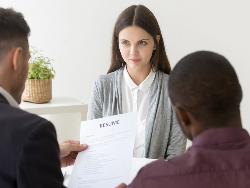 A job candidate facing two interviewers, with one holding a resume.