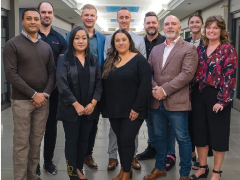 A group of professionals from the Manitoba Print Industry Association (MPIA) posing together at an industry event. The attendees are dressed in business attire and standing in a well-lit hallway.