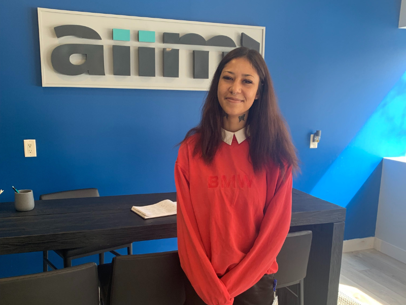 Savannah Hodder standing and smiling in front of the AIIM logo inside a modern office space.
