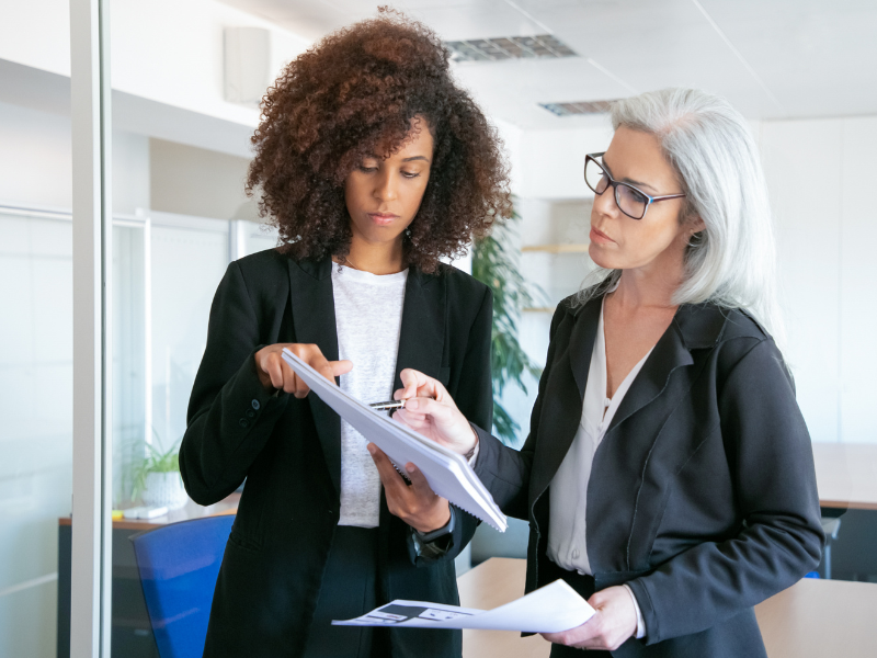 Two professional women reviewing documents in a modern office, representing fractional staffing collaboration in the print industry.