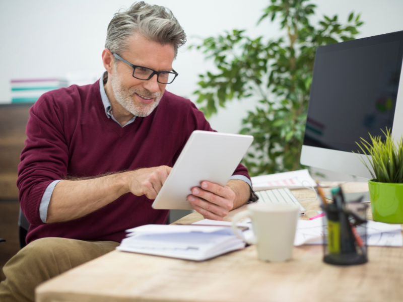 Mature business owner reviewing financial data on a tablet in a bright, modern office setting.