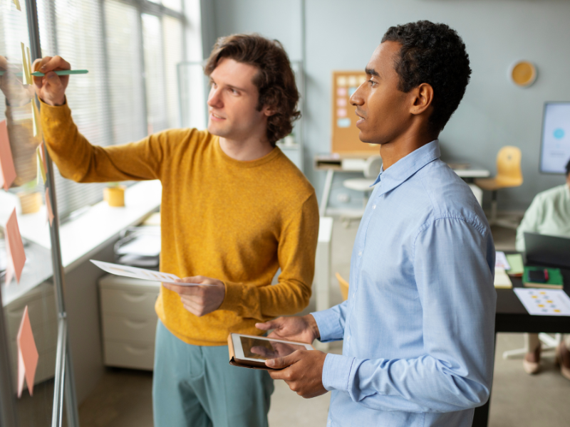 Two professionals collaborating in a modern office, using a whiteboard and digital tablet to plan business strategies.