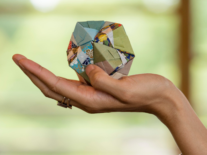 A hand holding a small, handcrafted paper object, symbolizing care, creativity, and sustainability in print solutions.
