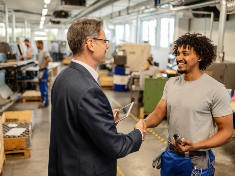 Business leader shaking hands with a skilled production employee on a modern print manufacturing floor.