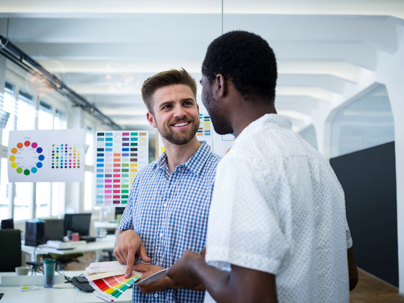Two print professionals reviewing color samples together in a production office, representing hands-on mentorship and knowledge transfer.
