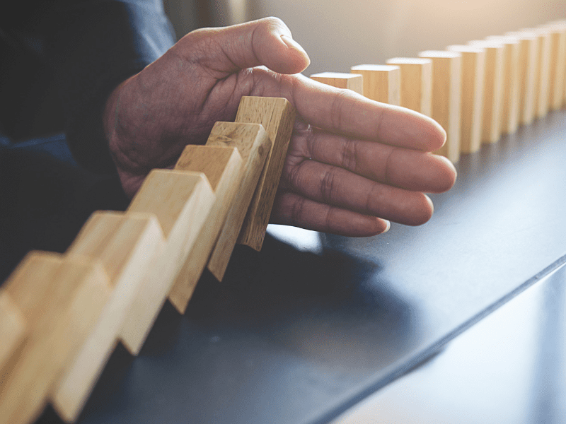 Hand stopping falling wooden dominoes, symbolizing business continuity planning and risk prevention in the printing and packaging industry.