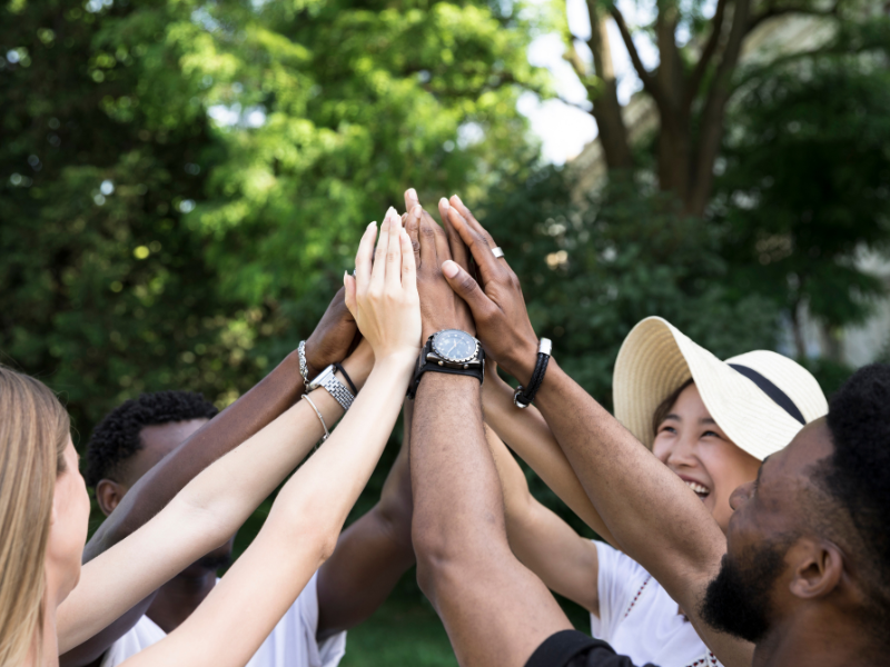 Diverse team joins hands outdoors, reflecting community engagement that strengthens print business culture and trust.