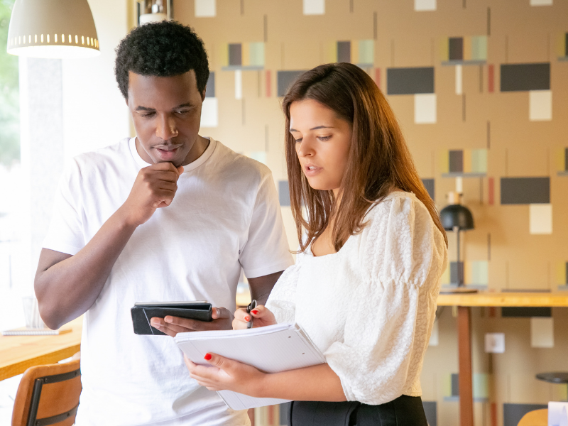 Two colleagues review figures on a tablet and notepad, reflecting pricing strategy decisions in a digital-age business.