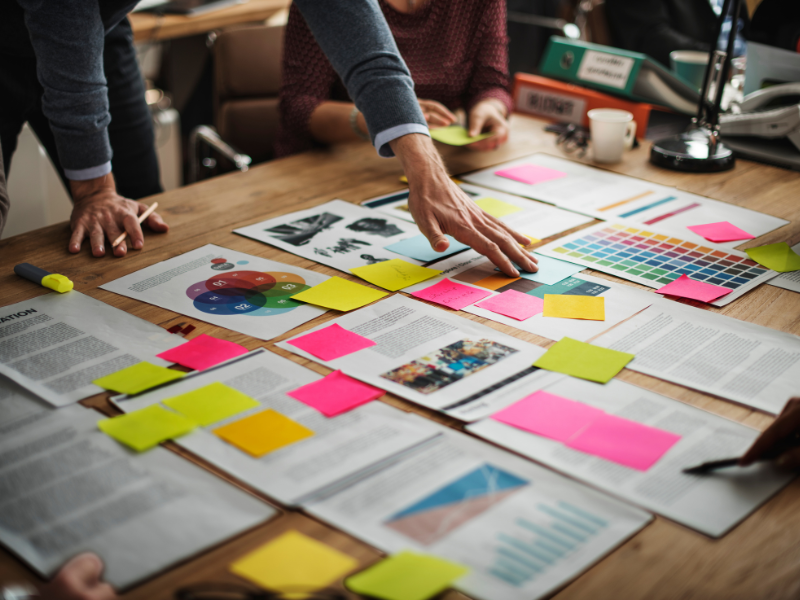 Team reviewing charts, print samples, and sticky notes during a scenario planning session for business strategy.