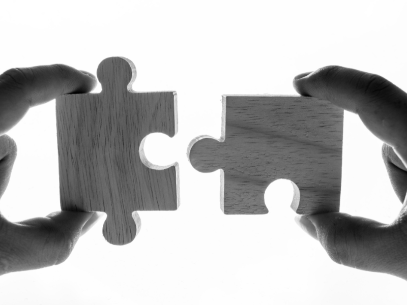 Hands holding two puzzle pieces about to connect, representing post-acquisition integration strategy