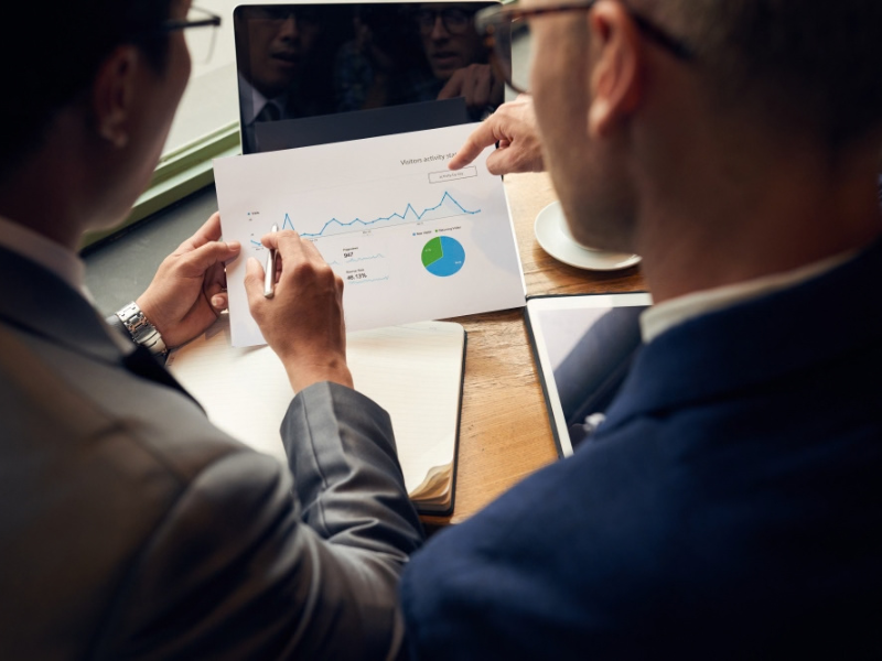 every capital investment needs a business thesis Two business leaders review performance charts while discussing a capital investment thesis for print operations.