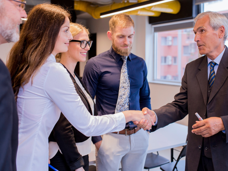 Executives shake hands during an acquisition meeting, reflecting M&A deal structure and risk allocation decisions.