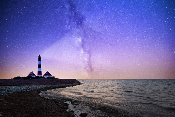A lighthouse on the coast with a purple sky overhead