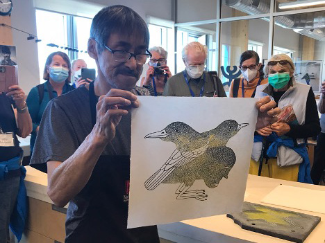 An Inuit man holding up a freshly made print of two birds.