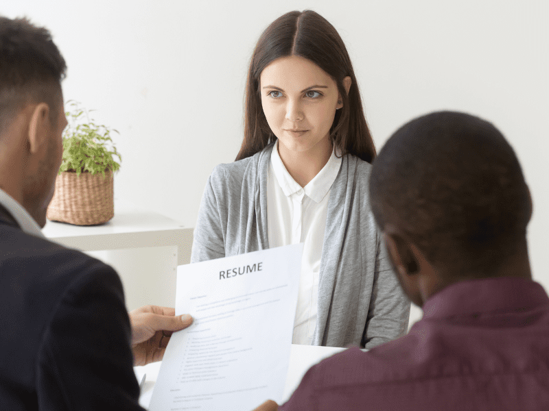 A job candidate facing two interviewers, with one holding a resume.