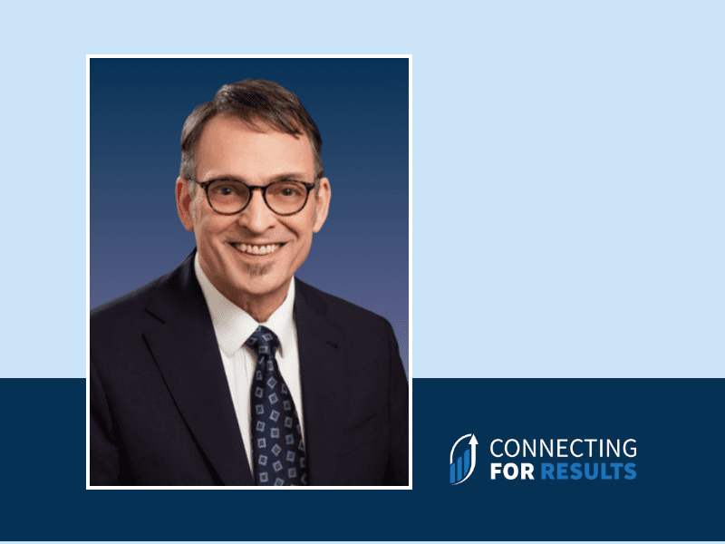 A professional headshot of Ron Boyle, a Revenue Specialist at Connecting for Results, wearing a dark suit, white shirt, and patterned tie, smiling against a blue gradient background.